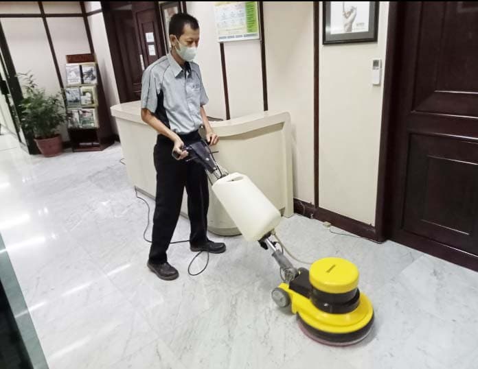 Petugas cleaning service memoles lantai marmer lobi dengan mesin polisher